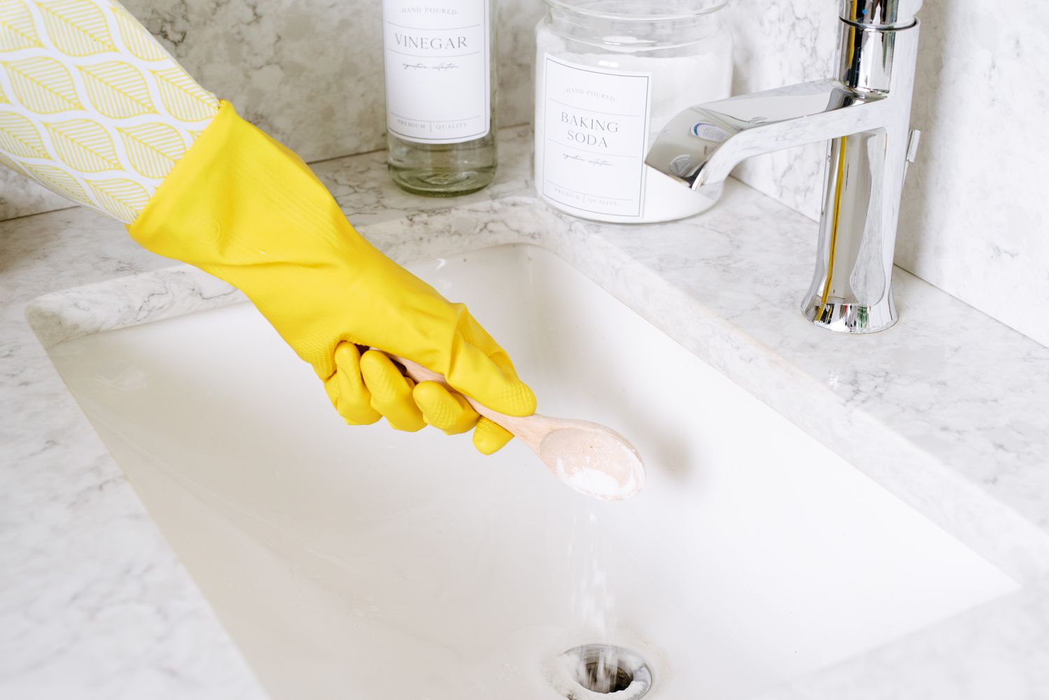 Hausgemachter Abflussreiniger mit Löffel und gelben Handschuhen in den Abfluss der Spüle gegossen