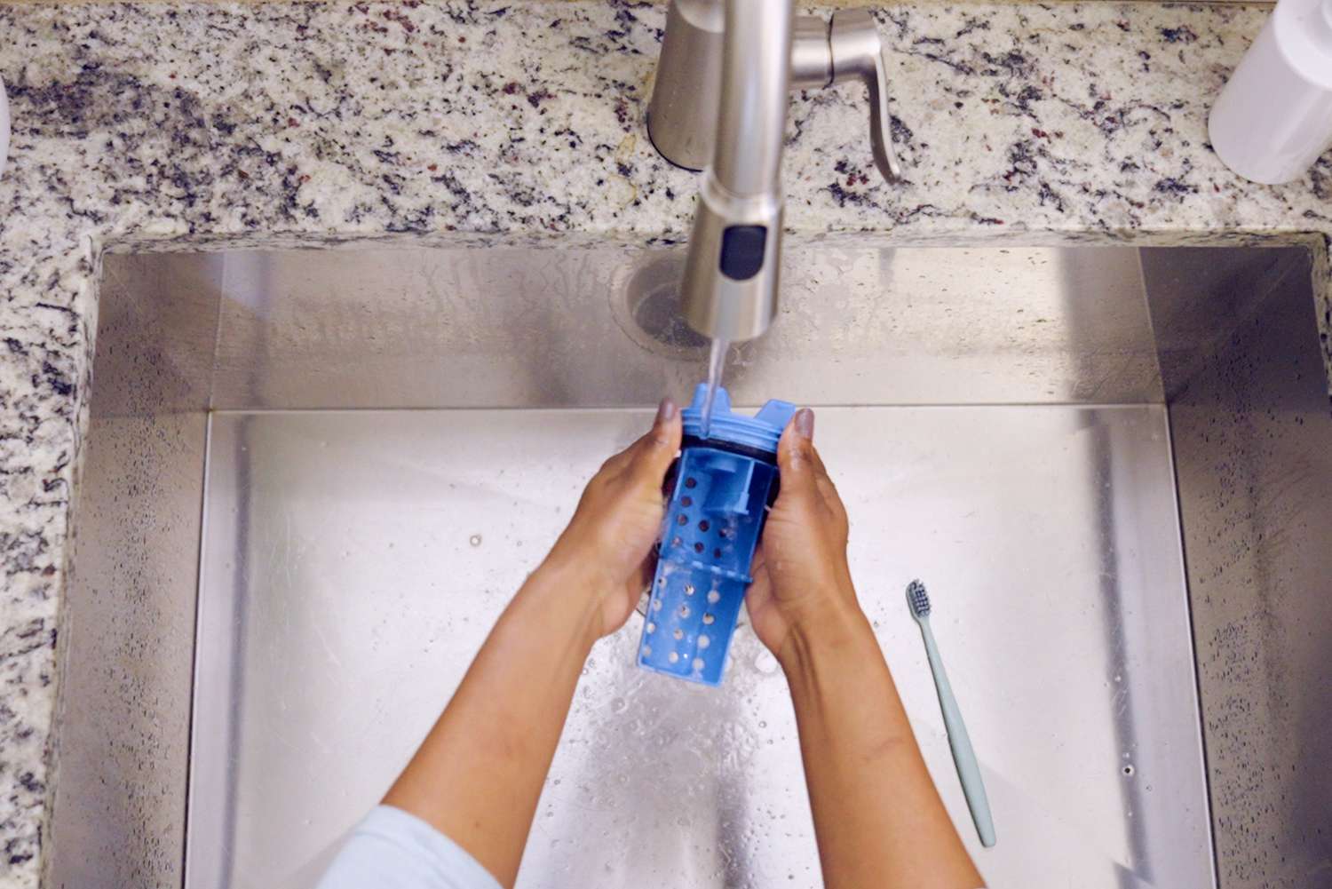 Blue drain line filter rinsed under running sink water by hang