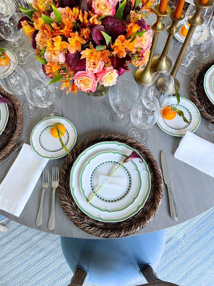 Gedeckter Tisch mit orangefarbenen, rosafarbenen und lilafarbenen Blumen, Kerzenständern aus Messing und orangefarbenen Kerzen sowie weißem und grünem Geschirr