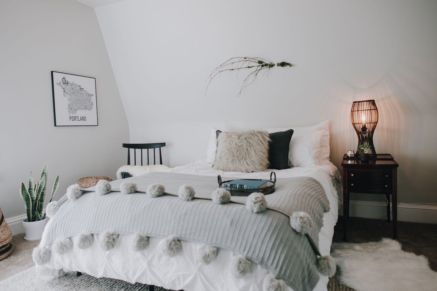 Modernes Schlafzimmer mit weichen Texturen: Plüschkissen, graue Decke mit Pompons am Ende. Kühle Töne