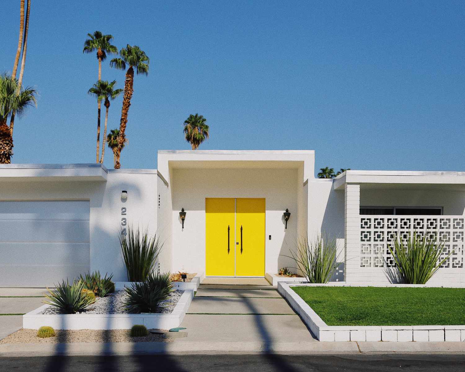 white house with yellow front door against a blue sky with palm trees