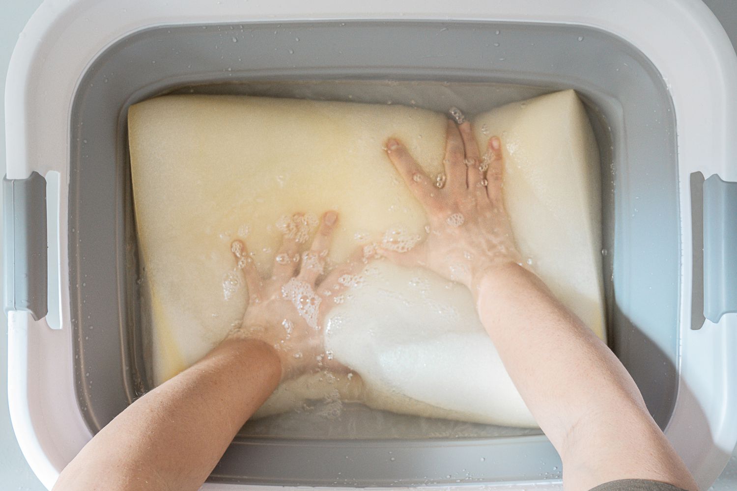 Gedächtnisschaumstoff-Kissen zur Reinigung in eine Wanne mit Wasser und Feinwaschmittel gegeben