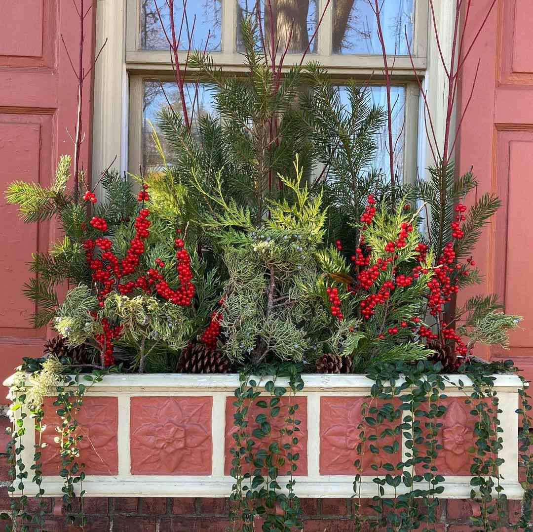 jardinera decorativa pintada en crema y terracota, con verdor invernal, bayas rojas y ramitas rojas