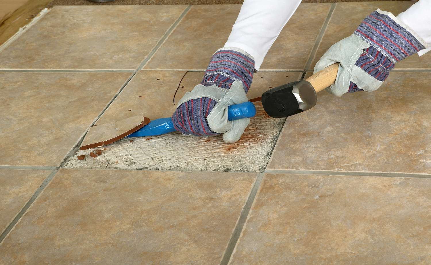 Homem usando martelo e cinzel para remover azulejo de mármore do piso, em close-up