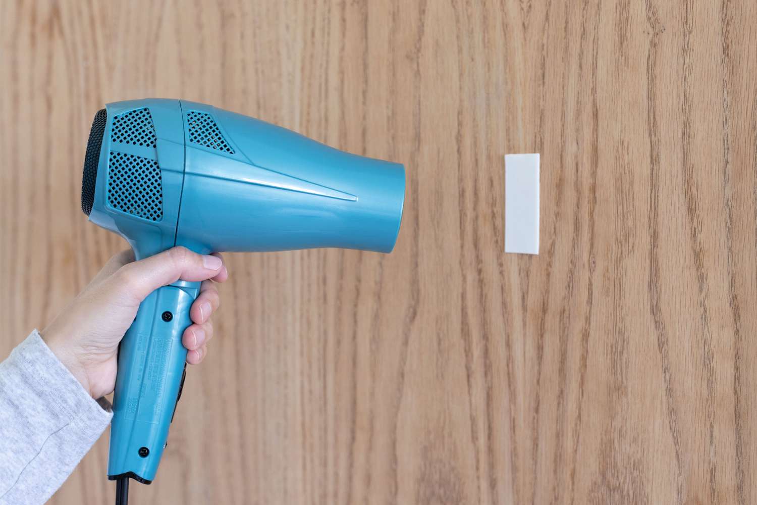 Secador de pelo azul soplando aire caliente sobre cinta de doble cara en pared de madera