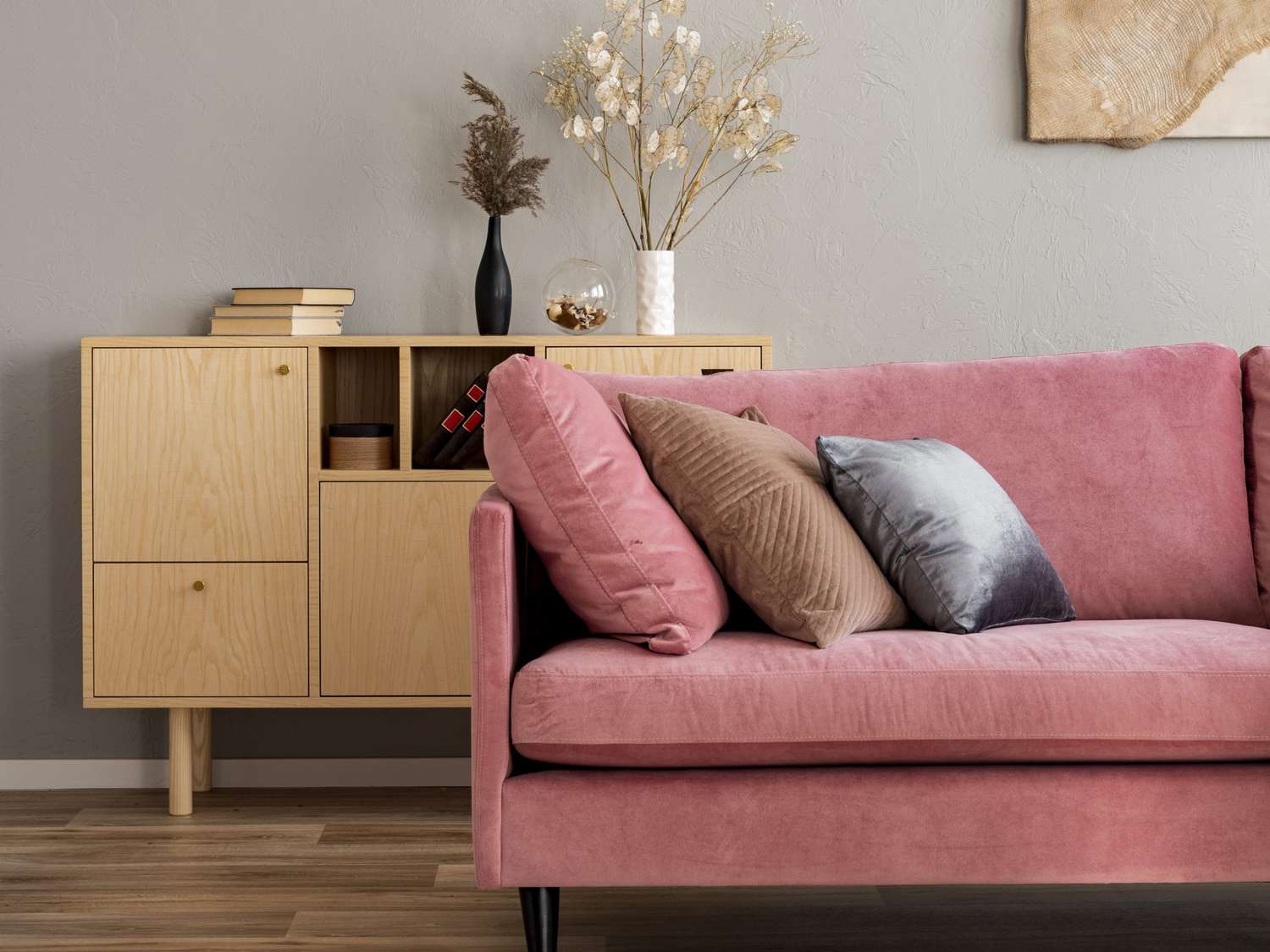 Blumen in Vasen auf hölzerner Kommode in zeitgenössischer Wohnzimmereinrichtung mit pastellrosa Sofa