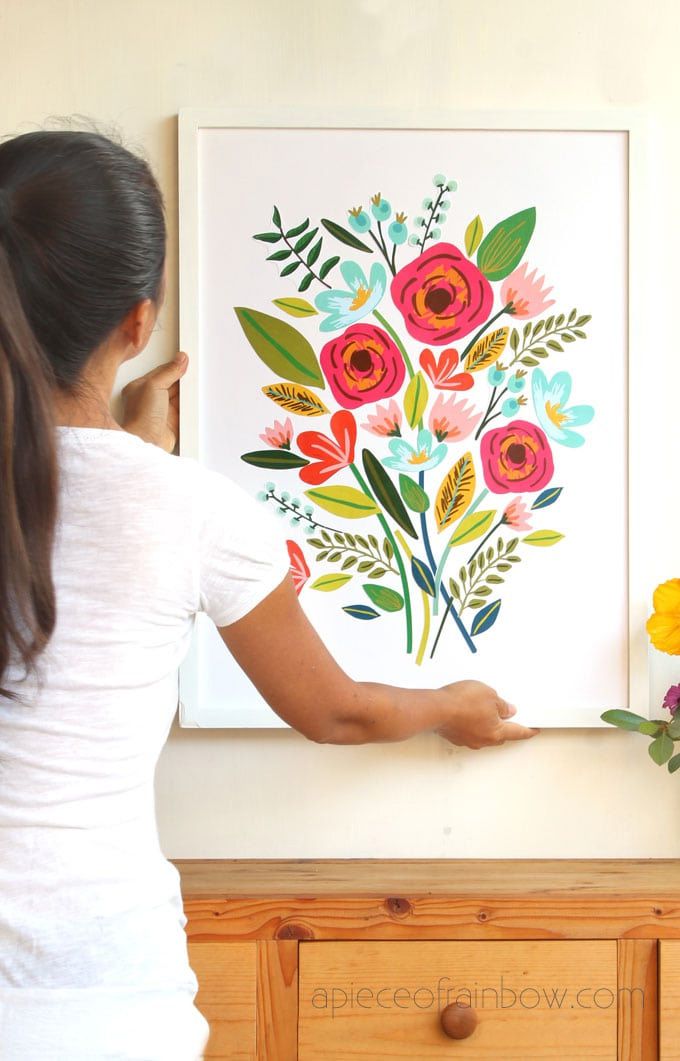 Una mujer colgando una obra de arte floral en la pared