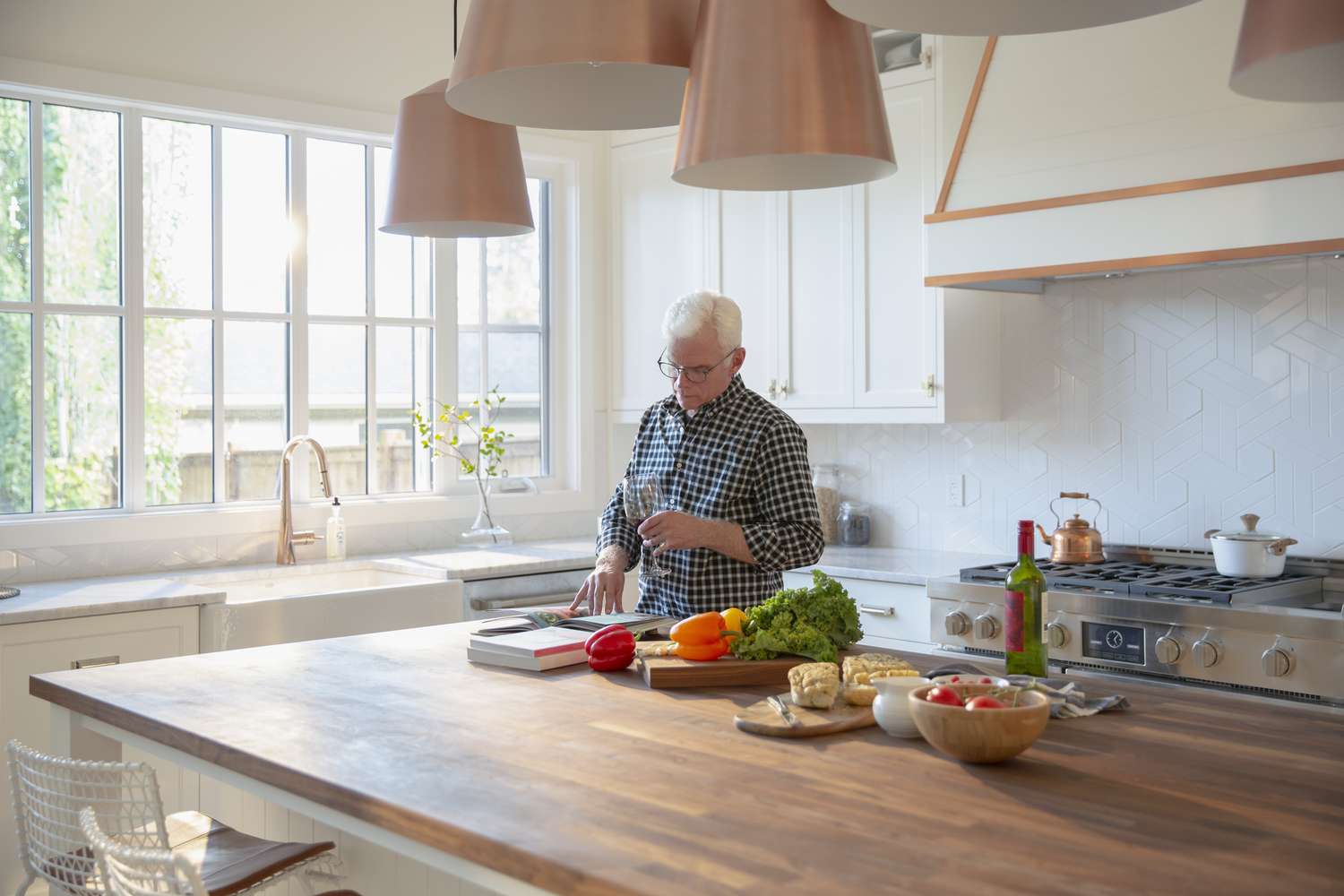 Hombre mayor cocinando, bebiendo vino y mirando un libro de cocina en la cocina