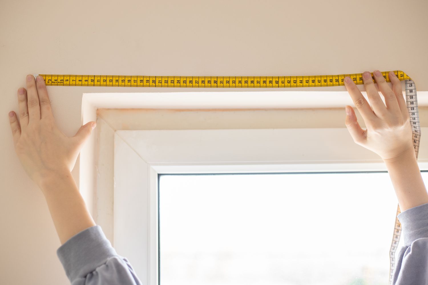 Fensterbreite wird mit gelbem Maßband für Jalousien gemessen