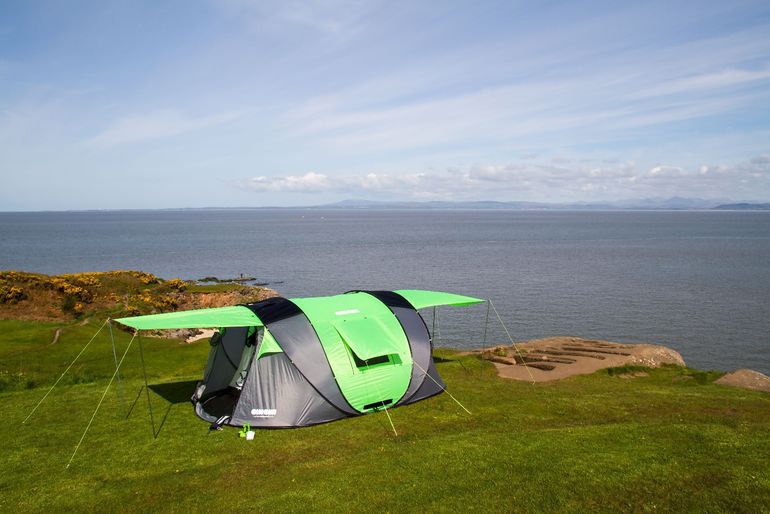 Längliches grünes und graues Zelt auf einer Hügelkuppe über dem Wasser