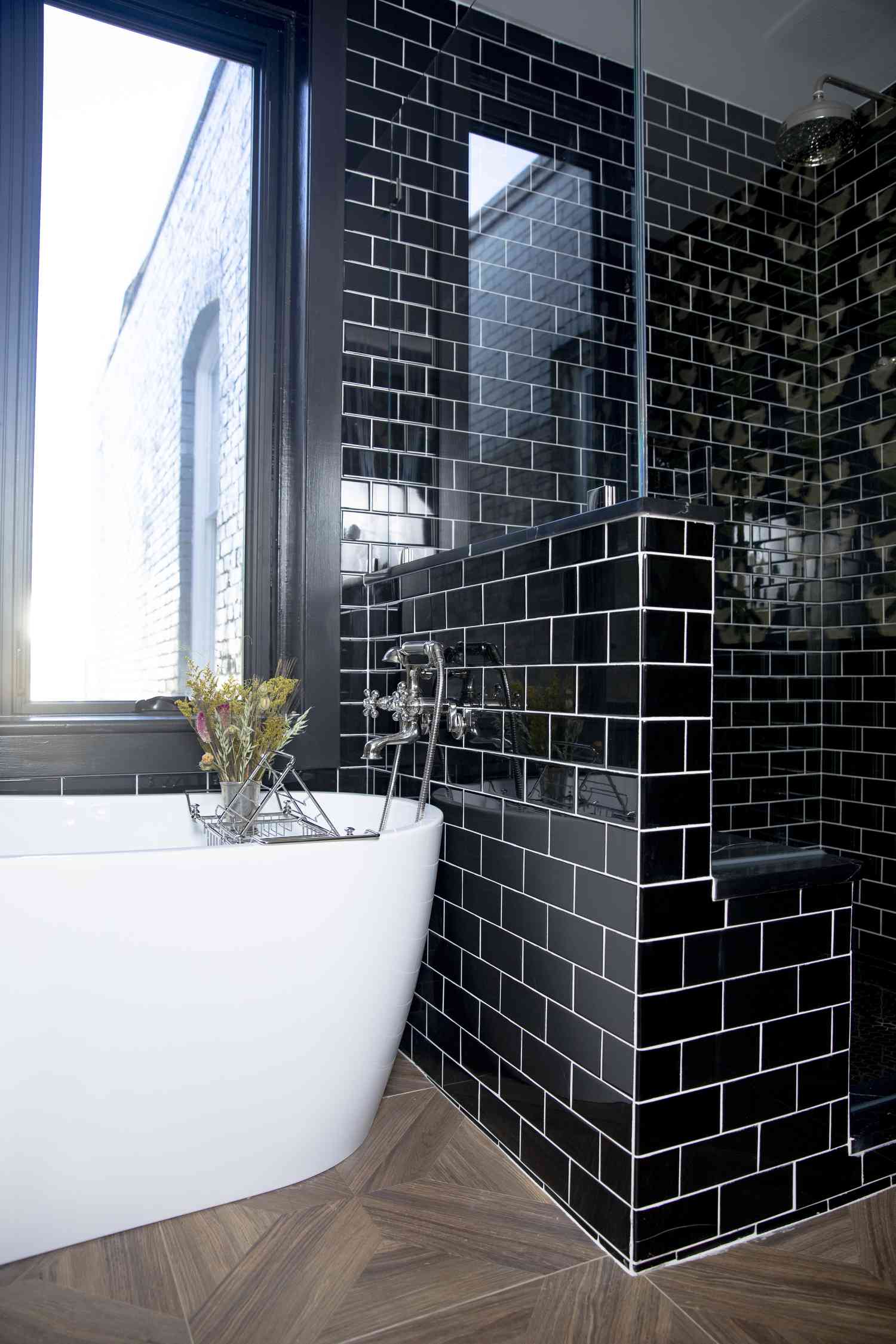 Banheiro com azulejos pretos e banheira branca independente.