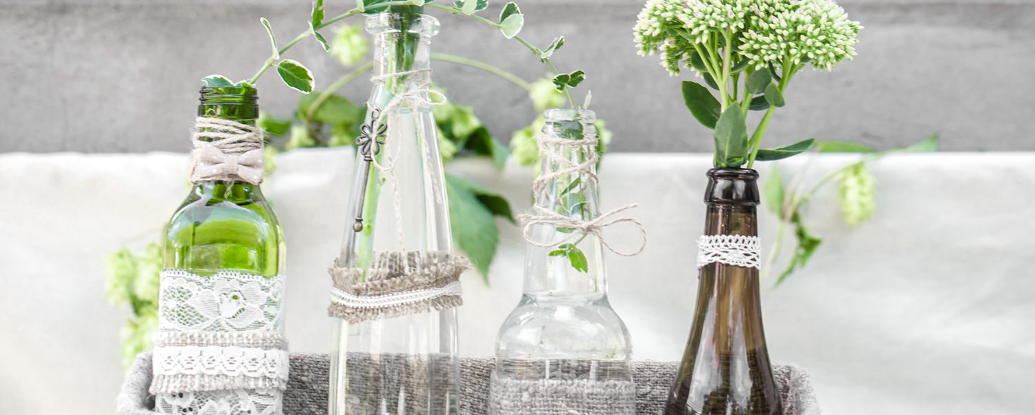 Centre de table composé de bouteilles enveloppées de dentelle et de ficelle et remplies de verdure