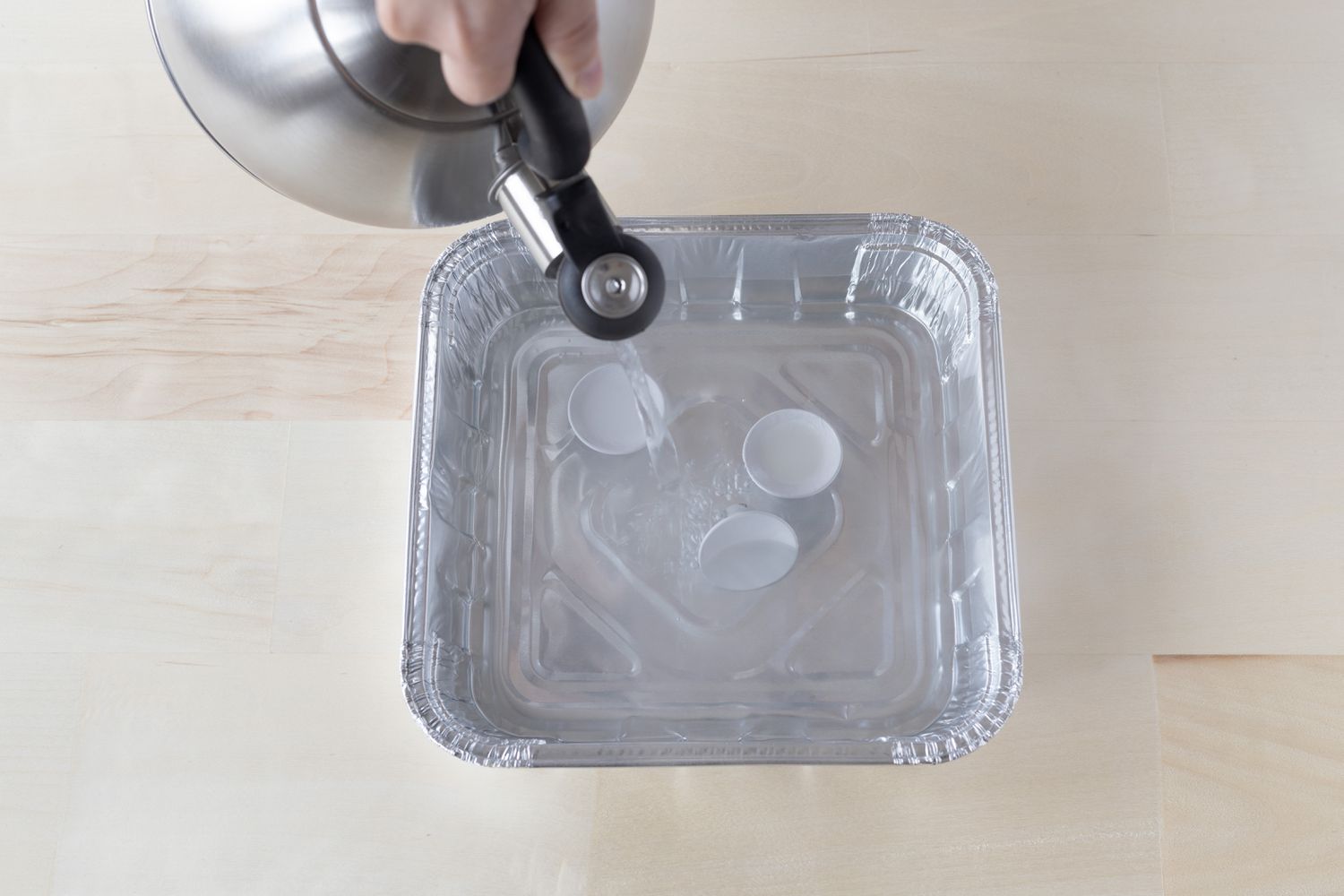 Água fervente da chaleira despejada em uma bandeja de alumínio descartável com botões de metal