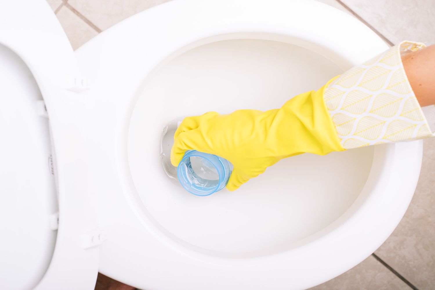 Weiße Keramiktoilette, die mit Wäscheflaschenverschluss und gelben Handschuhen Wasser ablässt
