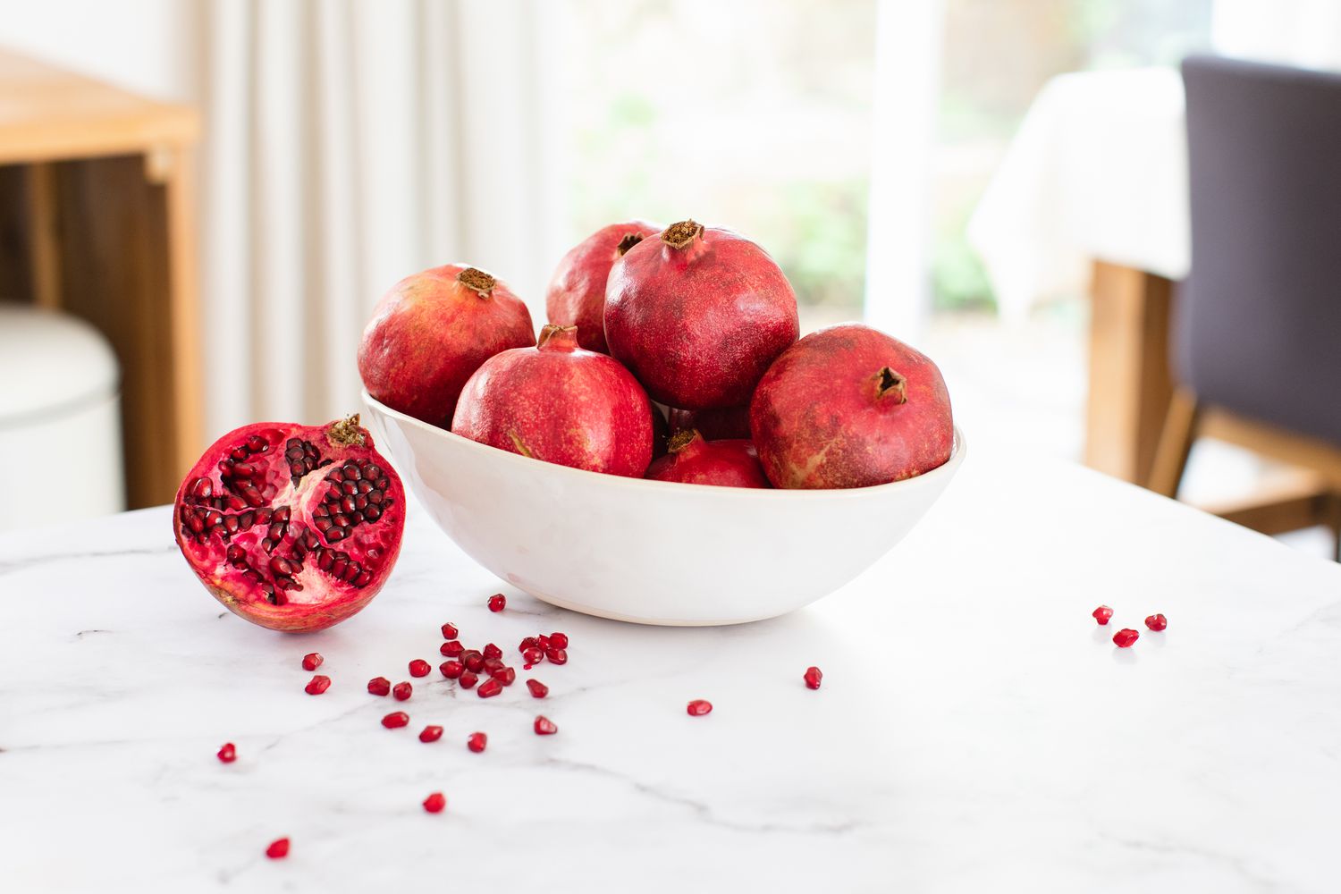 White ceramic bowl of pomegranates on kitchen counter top with seeds spread across