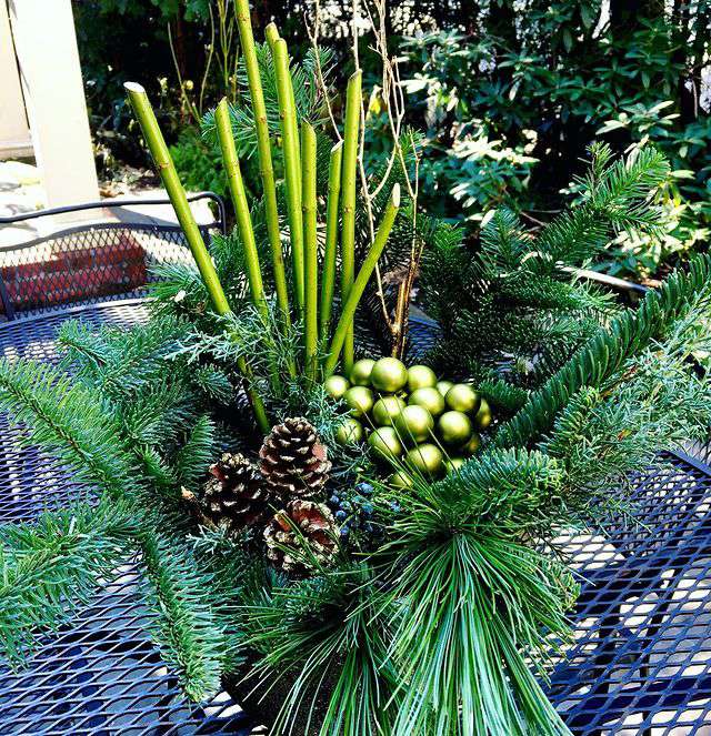 Winterarrangement mit Immergrün, Tannenzapfen, grünen Stängeln und grünem Weihnachtsschmuck aus Glas