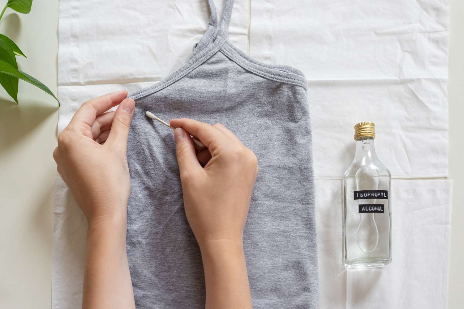 Cotonete aplicando álcool isopropílico em uma blusa de tanque dobrada sobre papel-toalha