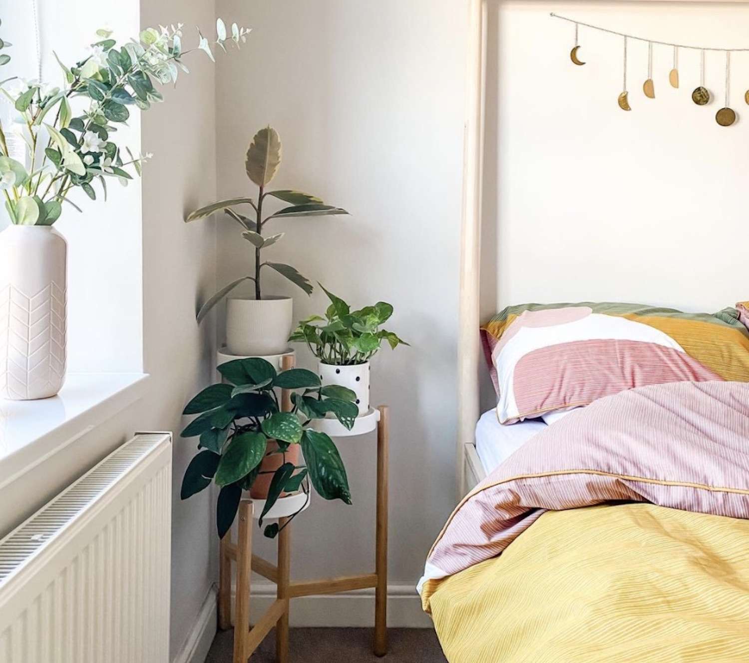 Modernes Schlafzimmer mit Pflanzen auf dem Nachttisch, gelbe und rosa Bettdecke