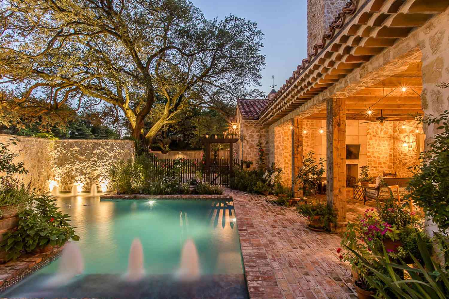 Mediterraner Pool mit Steinsteg, großem Baum und kleinen Springbrunnen.