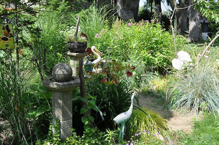 Jardín junto a la playa con estatuas de garceta y pelícano, pilares de piedra y hierbas autóctonas