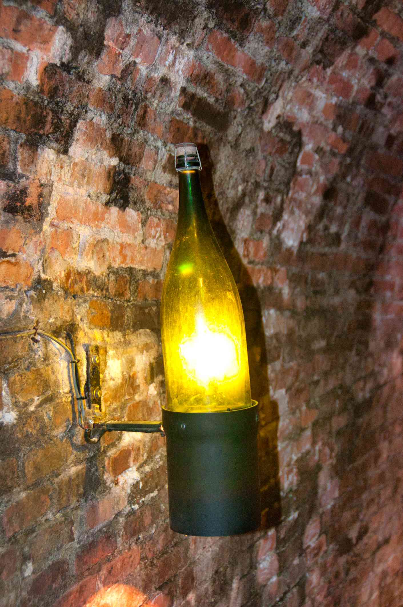 Botella de vino utilizada como candelabro en una pared de ladrillo