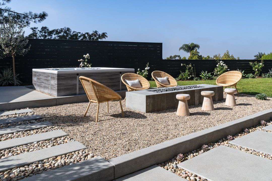 Graue Granitplatten und Kies in zwei Größen in einem Terrassensitzbereich mit Feuerstelle und Korbstühlen