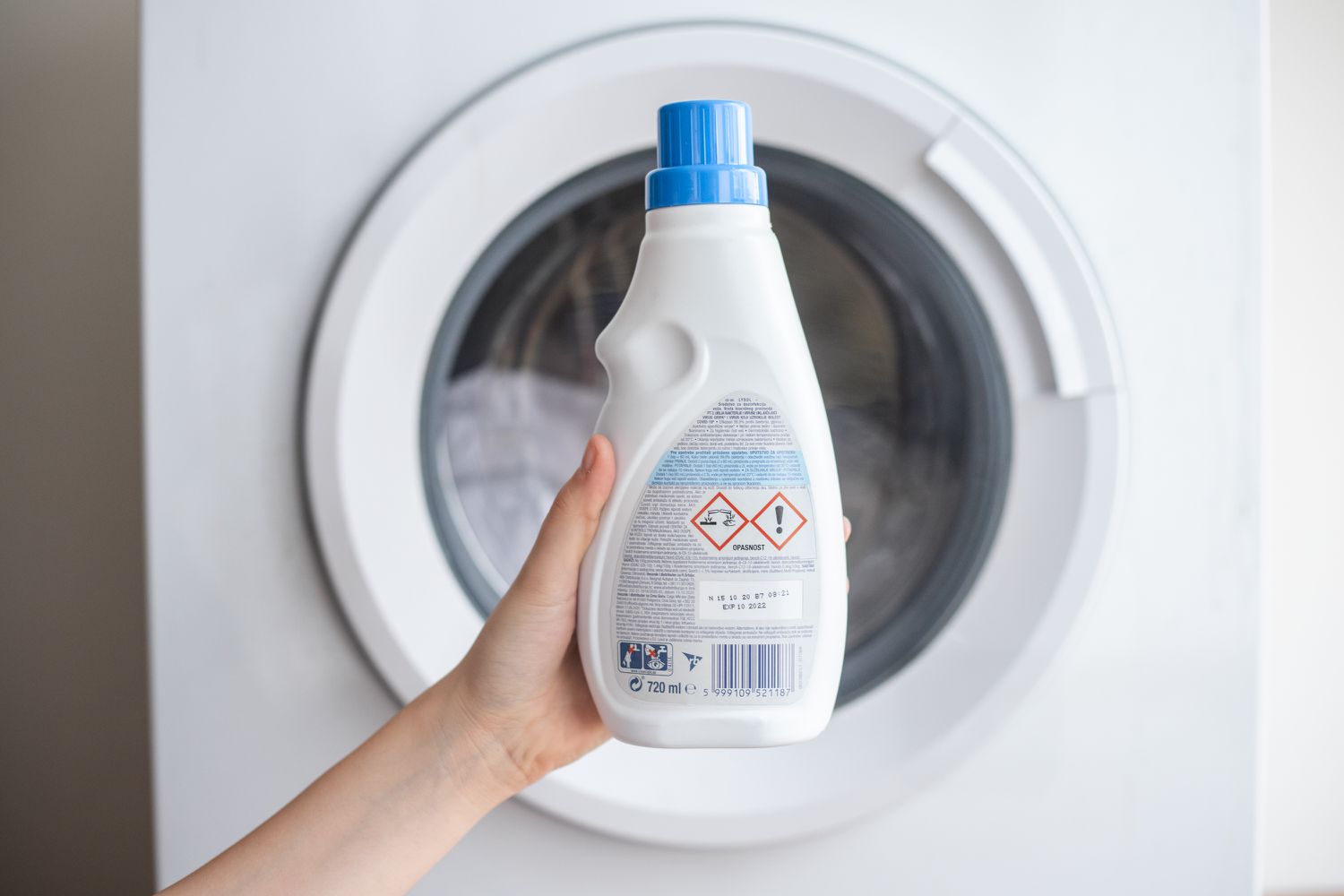 Heavy duty detergent with enzymes held up in front of washing machine