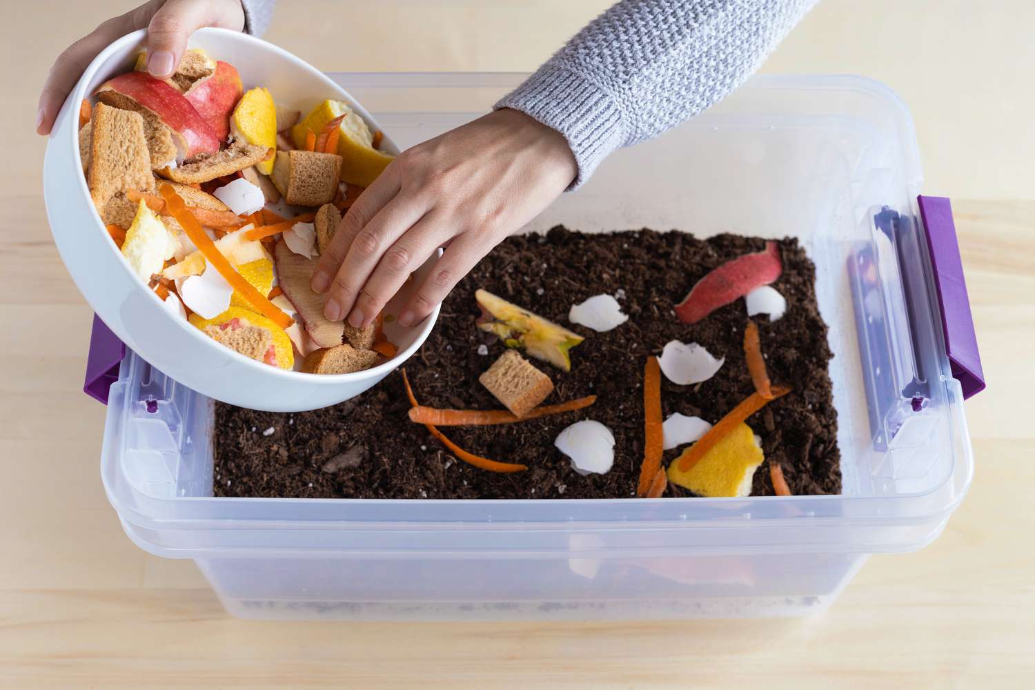 Essensreste, die zur Kompostierung in einen Plastikeimer mit Erde gefüllt werden