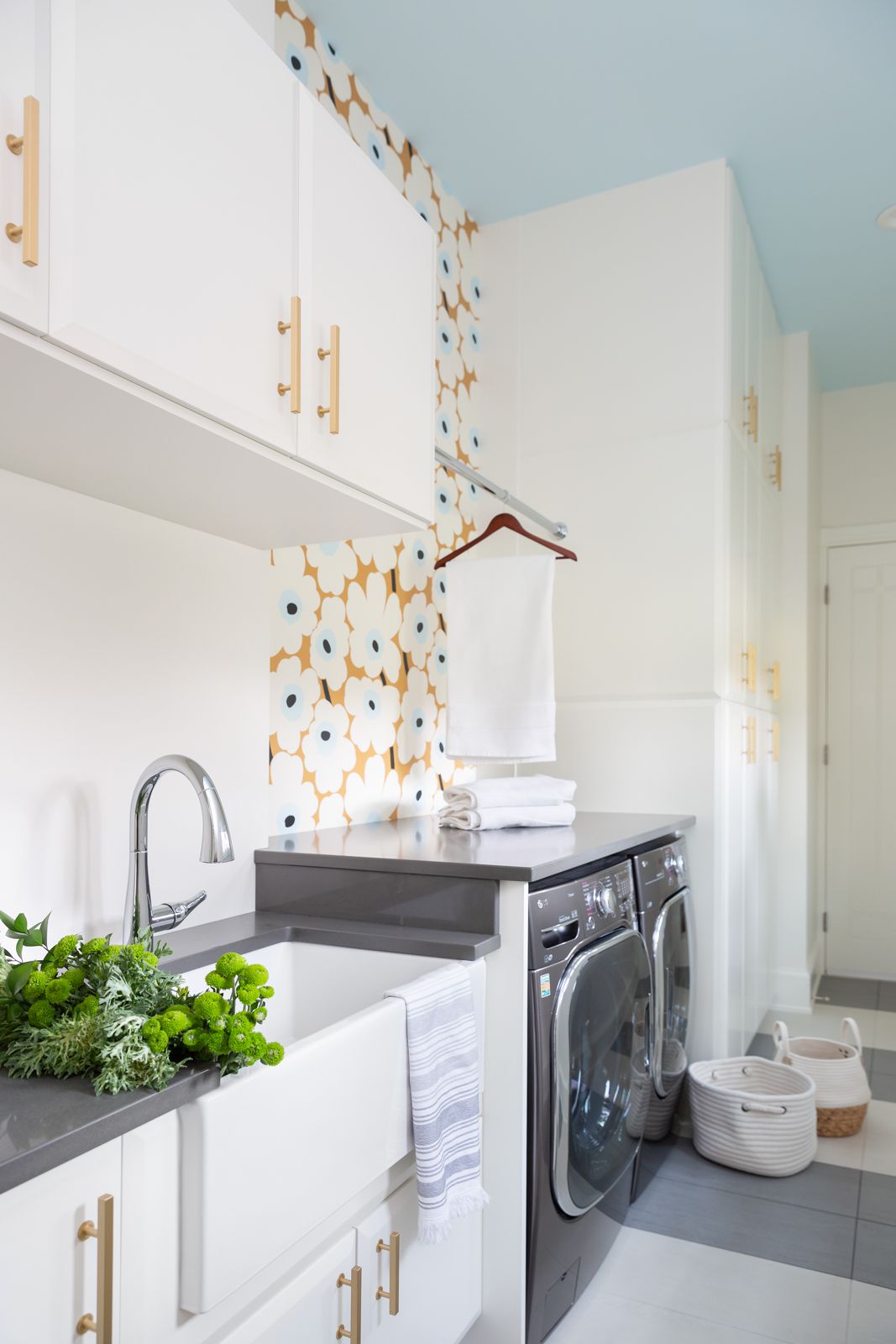 Eine Waschküche mit gelber Blümchentapete, grauen und weißen Fliesenböden und einer hellblauen Akzentdecke