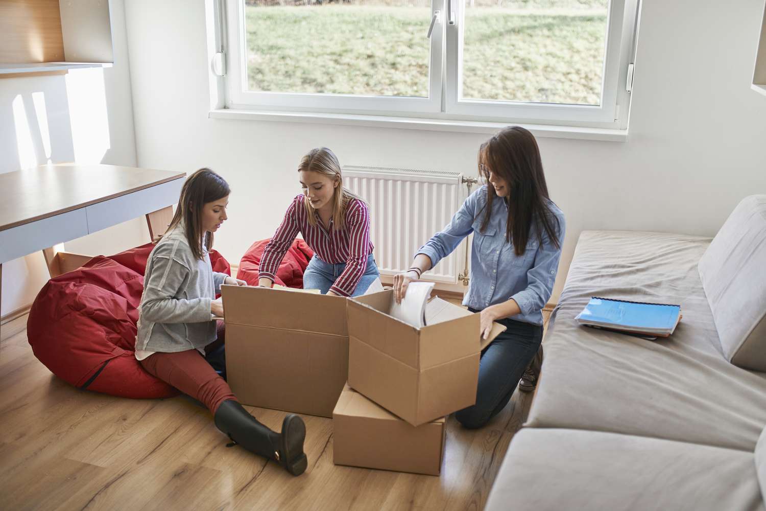 Três mulheres jovens desempacotando caixas de papelão em um quarto