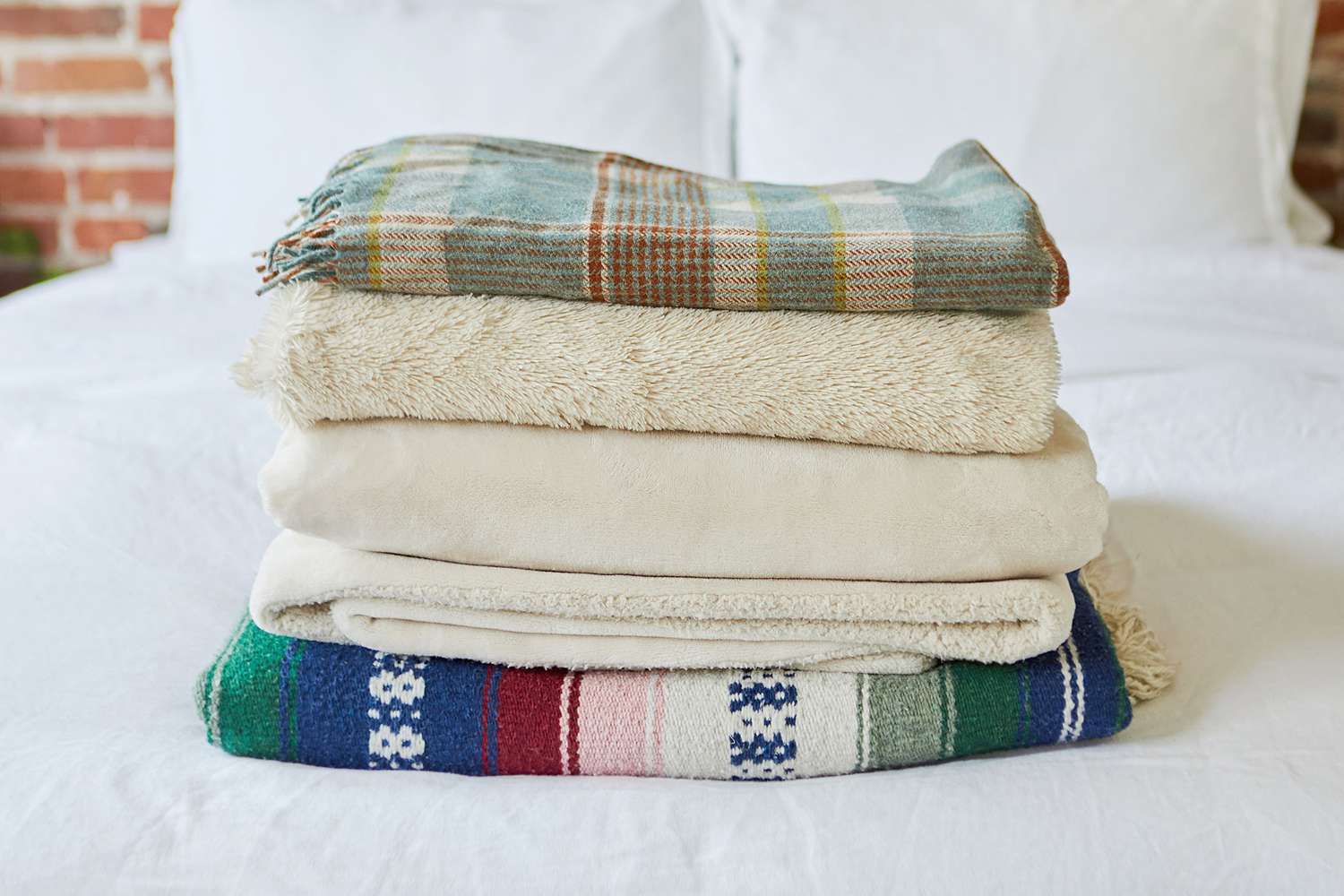 Cobertores estampados e de cor creme dobrados em cima de lençóis brancos