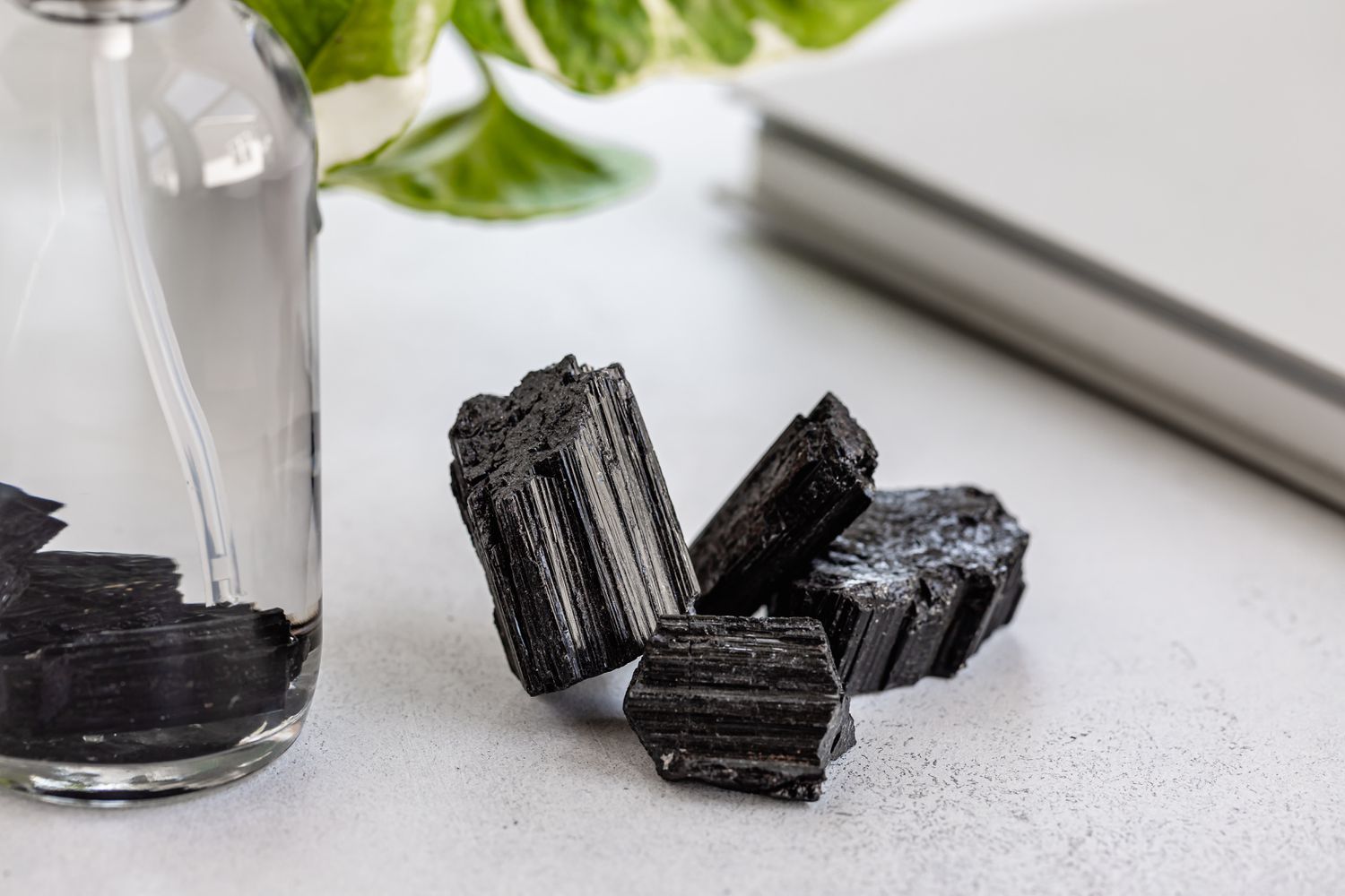 Piedras de turmalina negra junto a botella de spray con piedras dentro