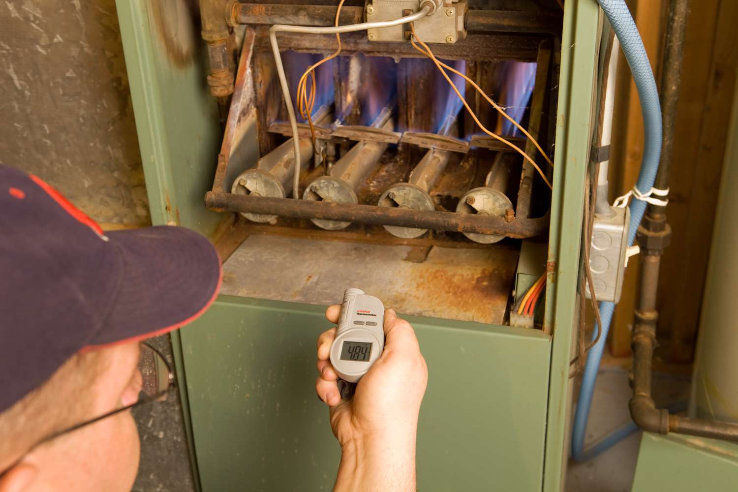 Monteur mit digitalem Infrarotthermometer prüft Ausgangstemperatur des Gasofens