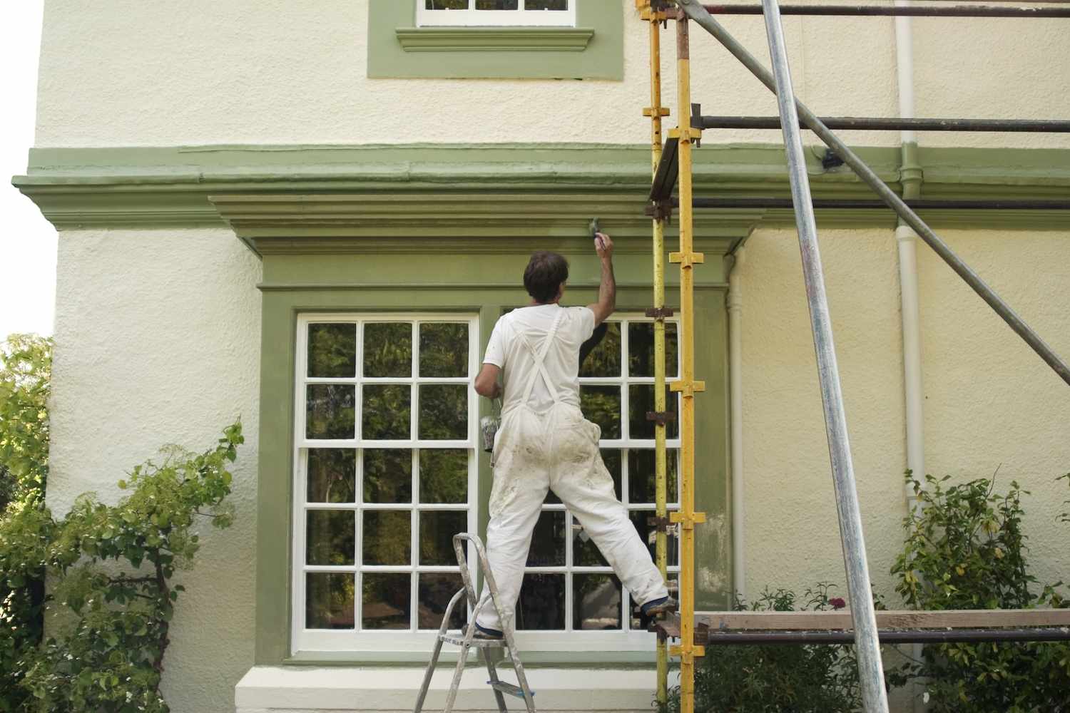 Pintor de casas sobre andamio pintando molduras verdes del exterior de la casa 