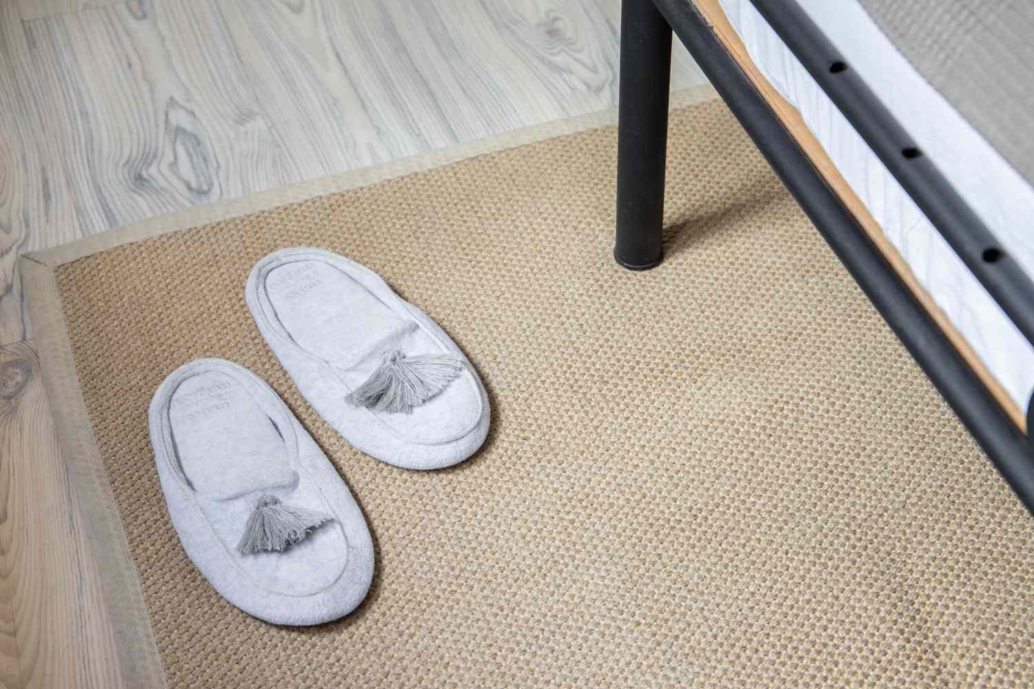 Tan rug with gray slippers on top underneath bed frame
