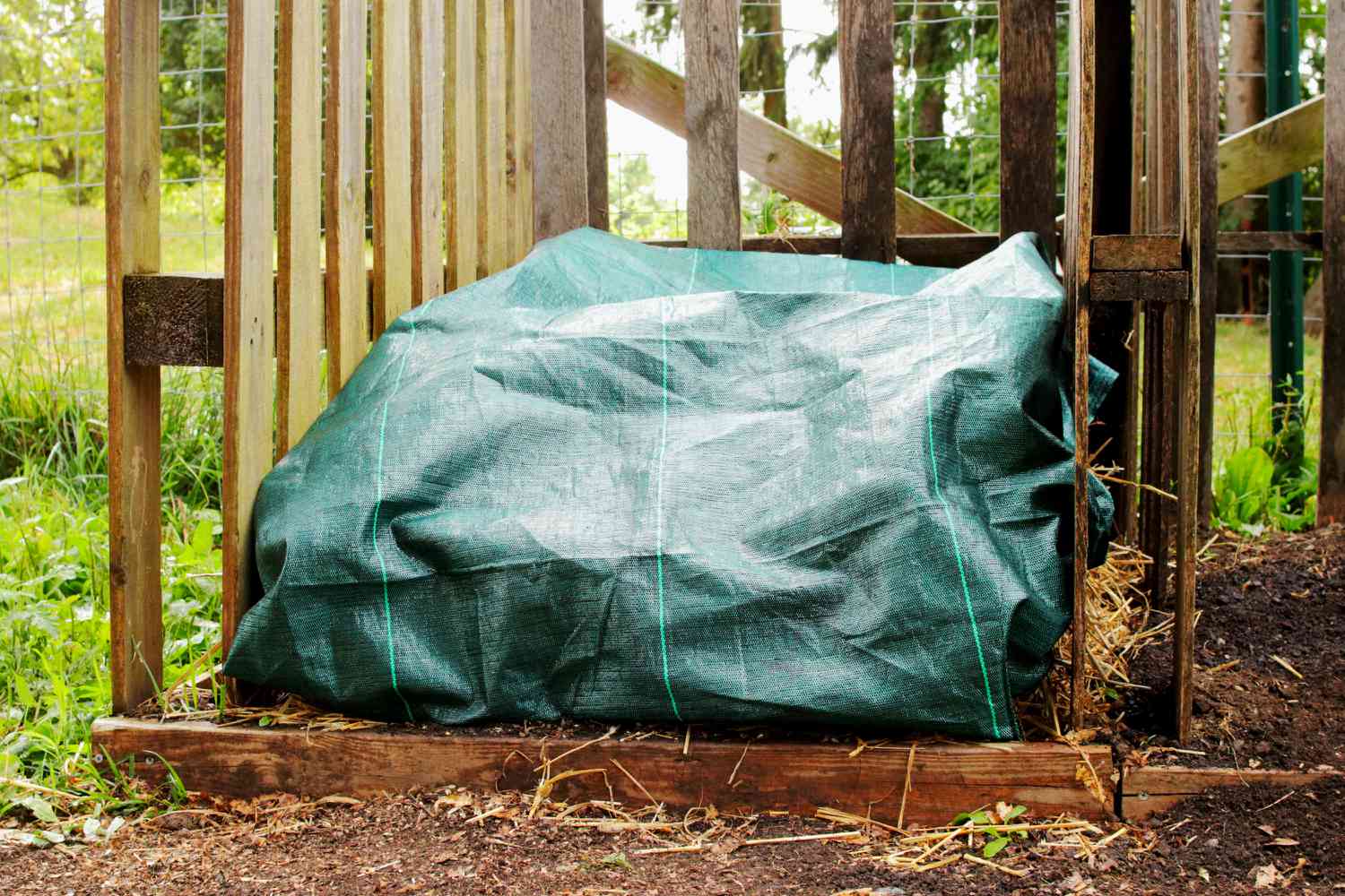 Pila de compost cubierta con malla verde en un cubo de madera