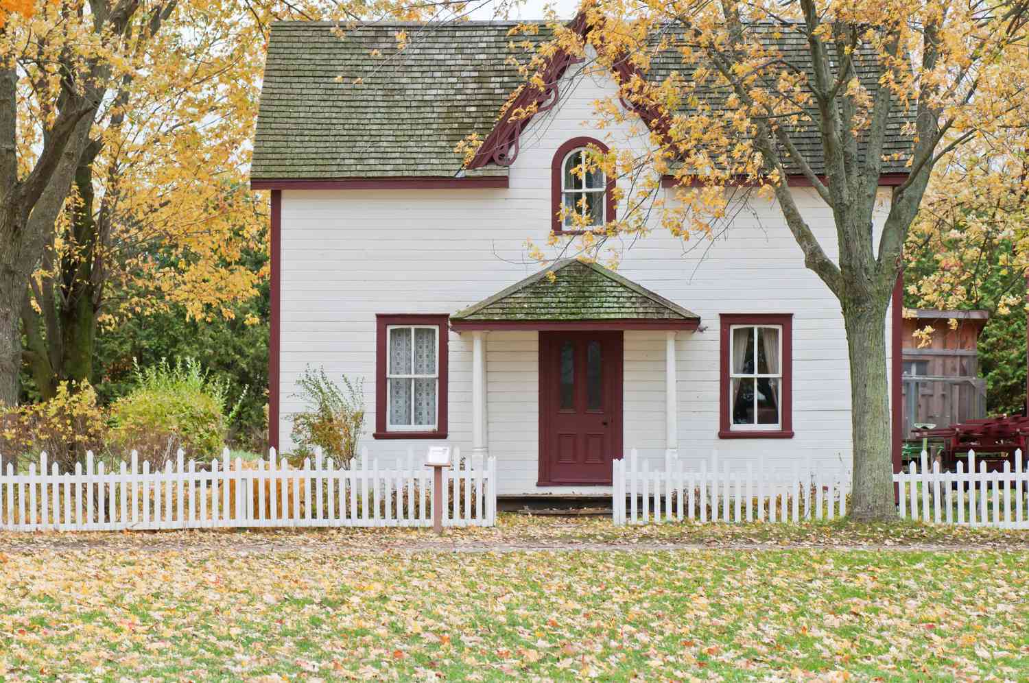 Una casita con un árbol y una valla en otoño