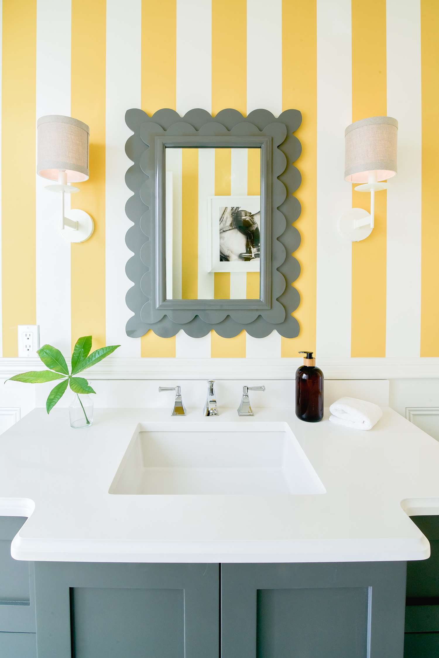 Um espelho cinza com vieiras contra uma parede listrada em um banheiro