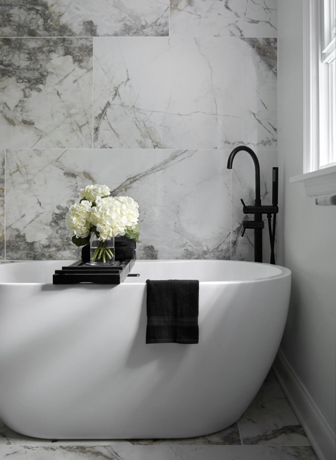 Graues und weißes Badezimmer mit weißer freistehender Wanne und großen Marmorfliesenwänden