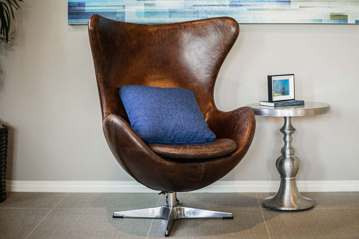 Brown leather Arne Jacobsen egg chair with blue throw pillow