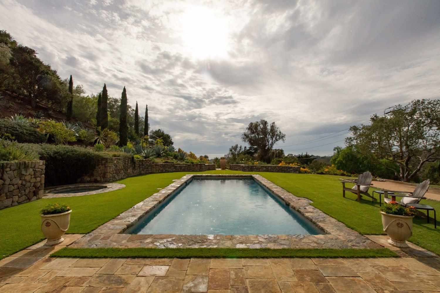 Mediterraner Swimmingpool mit Rasenfläche gegen bewölkten Himmel.