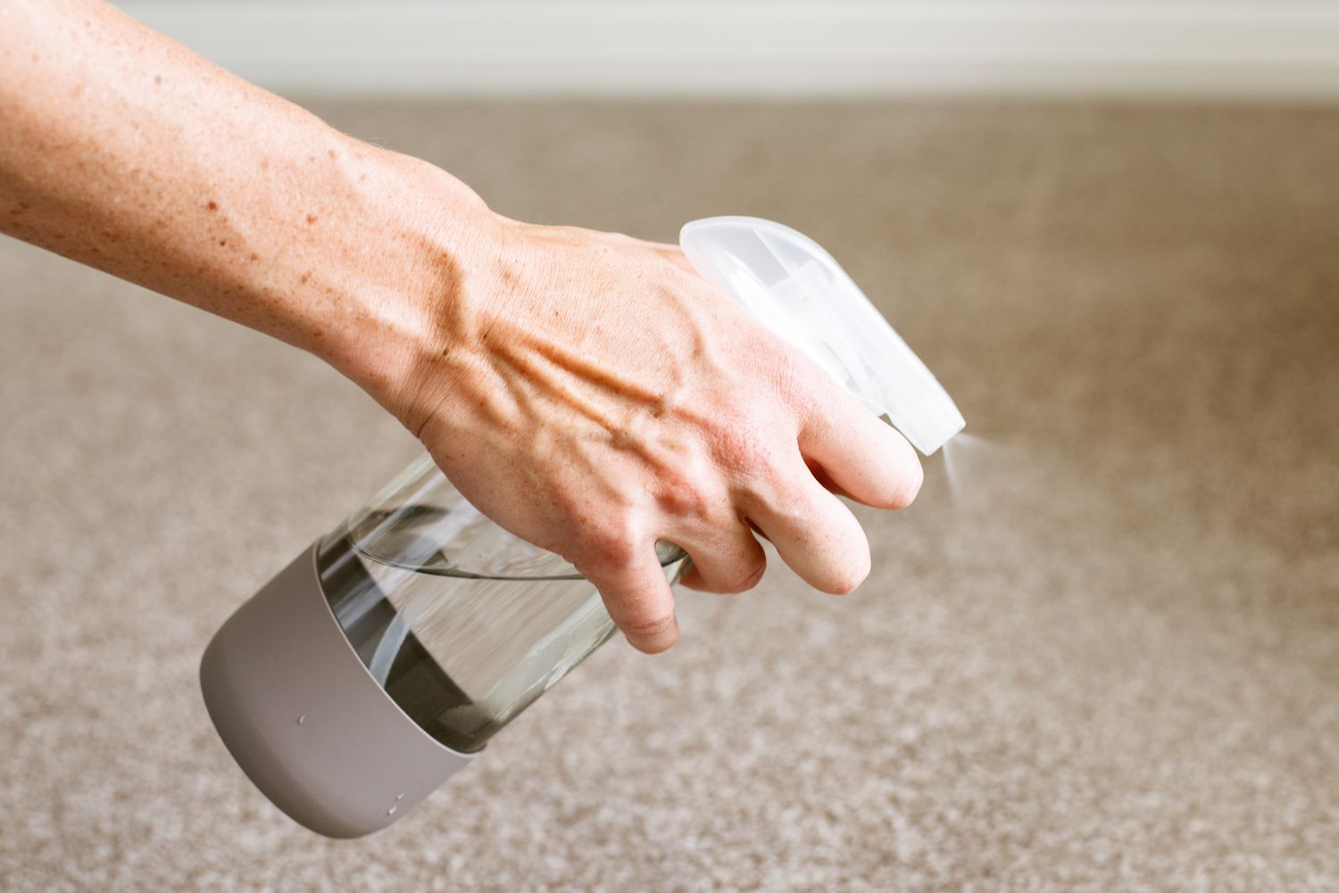 Glass spray bottle spraying solution over carpet until its damp