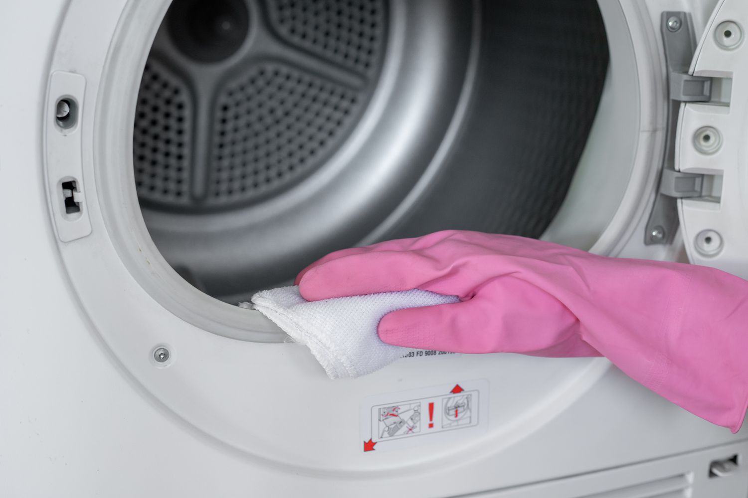 Tambor de la secadora limpiado con un paño humedecido en solución de cloro con guantes rosas