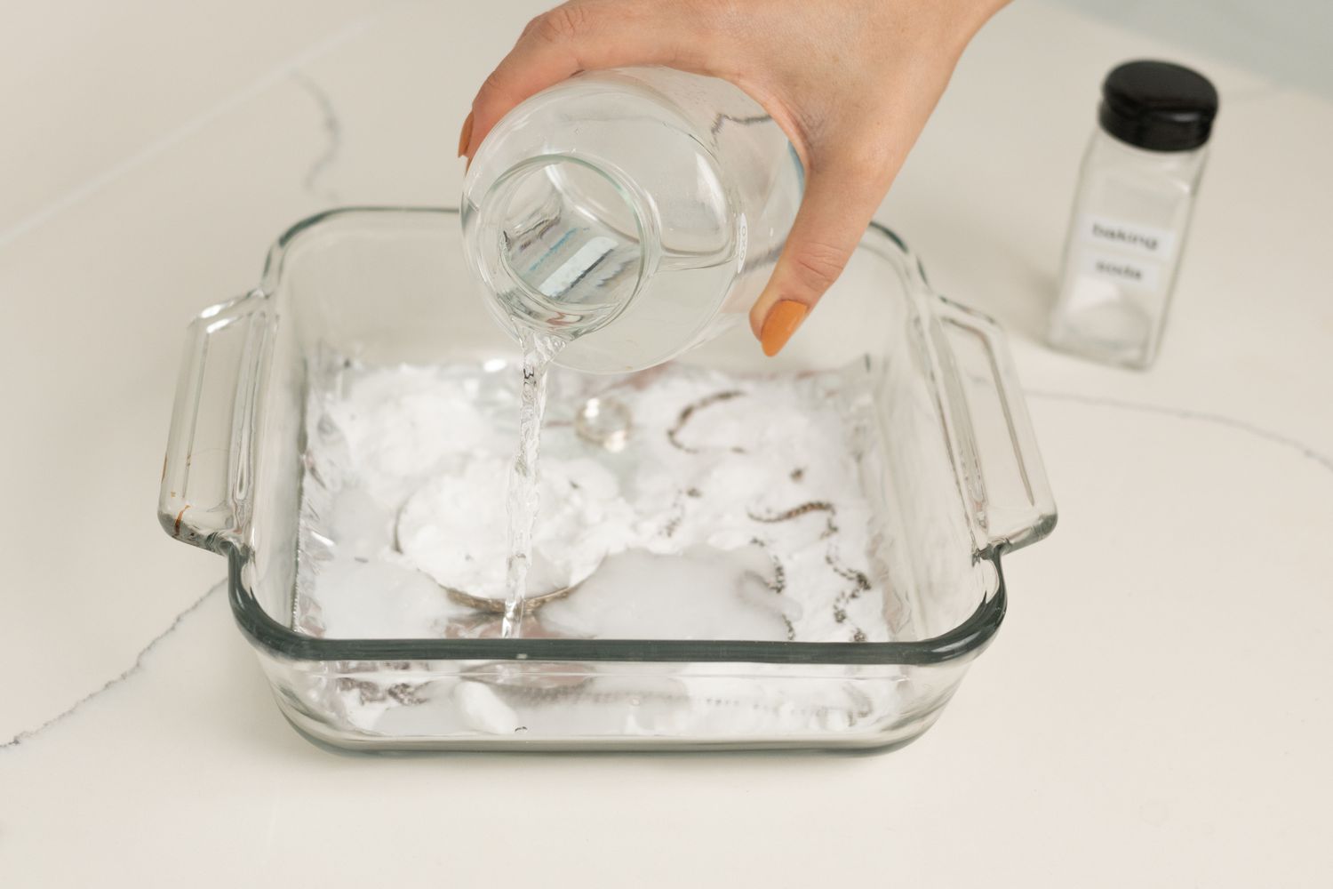 Heißes Wasser, das in eine Glasbackform gegossen wird, in der sich Backpulver und Alufolie vermischen