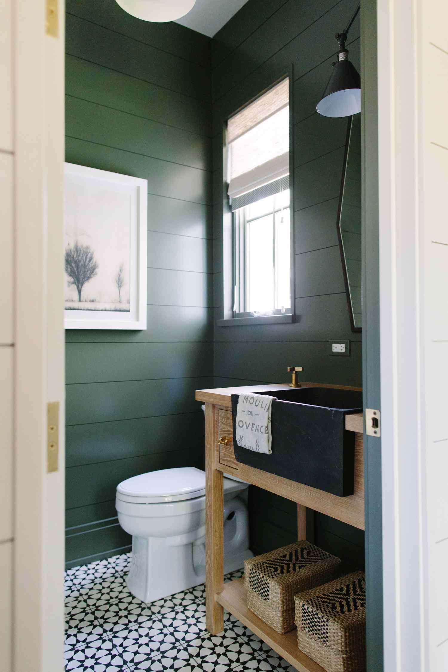 Um banheiro verde-escuro com pia preta e penteadeira de madeira