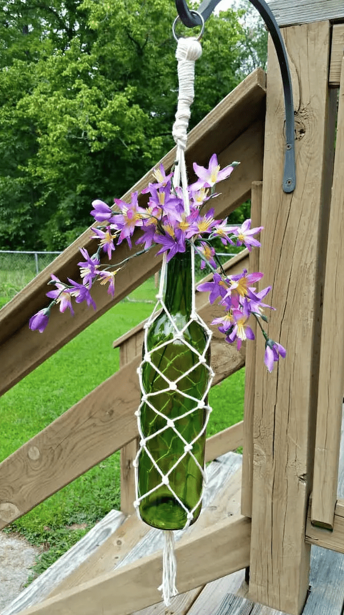 Weinflasche mit lila Blumen in einem Makramee-Halter