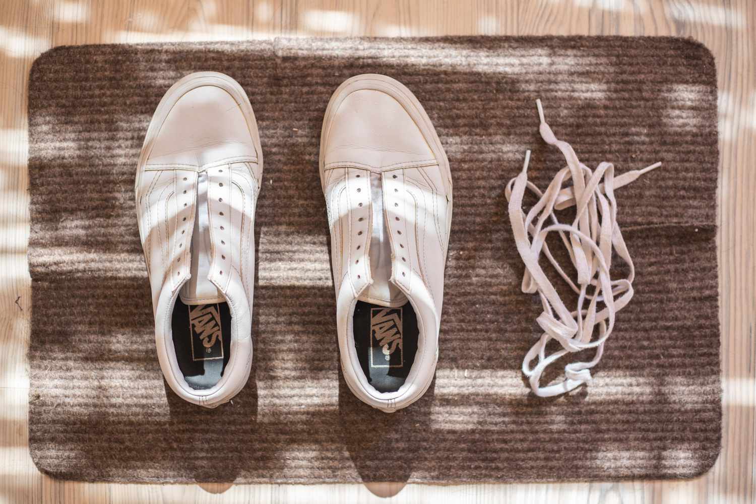 White leather Vans laid on brown rug to air dry outside next to laces