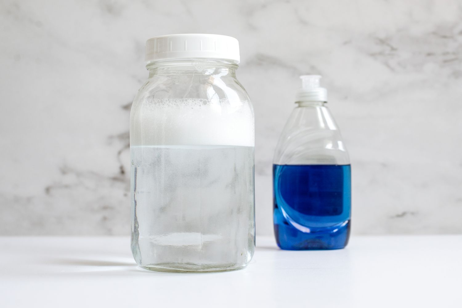 Botella grande transparente con agua y espuma de jabón delante de la botella de jabón líquido lavavajillas