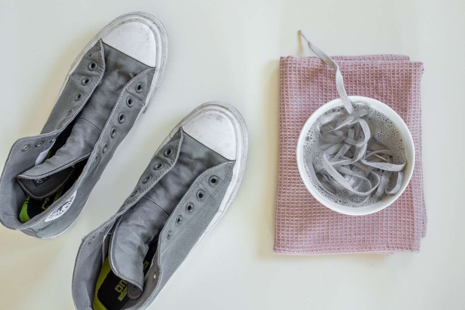 Schmutzige Schnürsenkel in einer kleinen Schüssel mit Seifenwasser neben grauen Converse-Sneakers