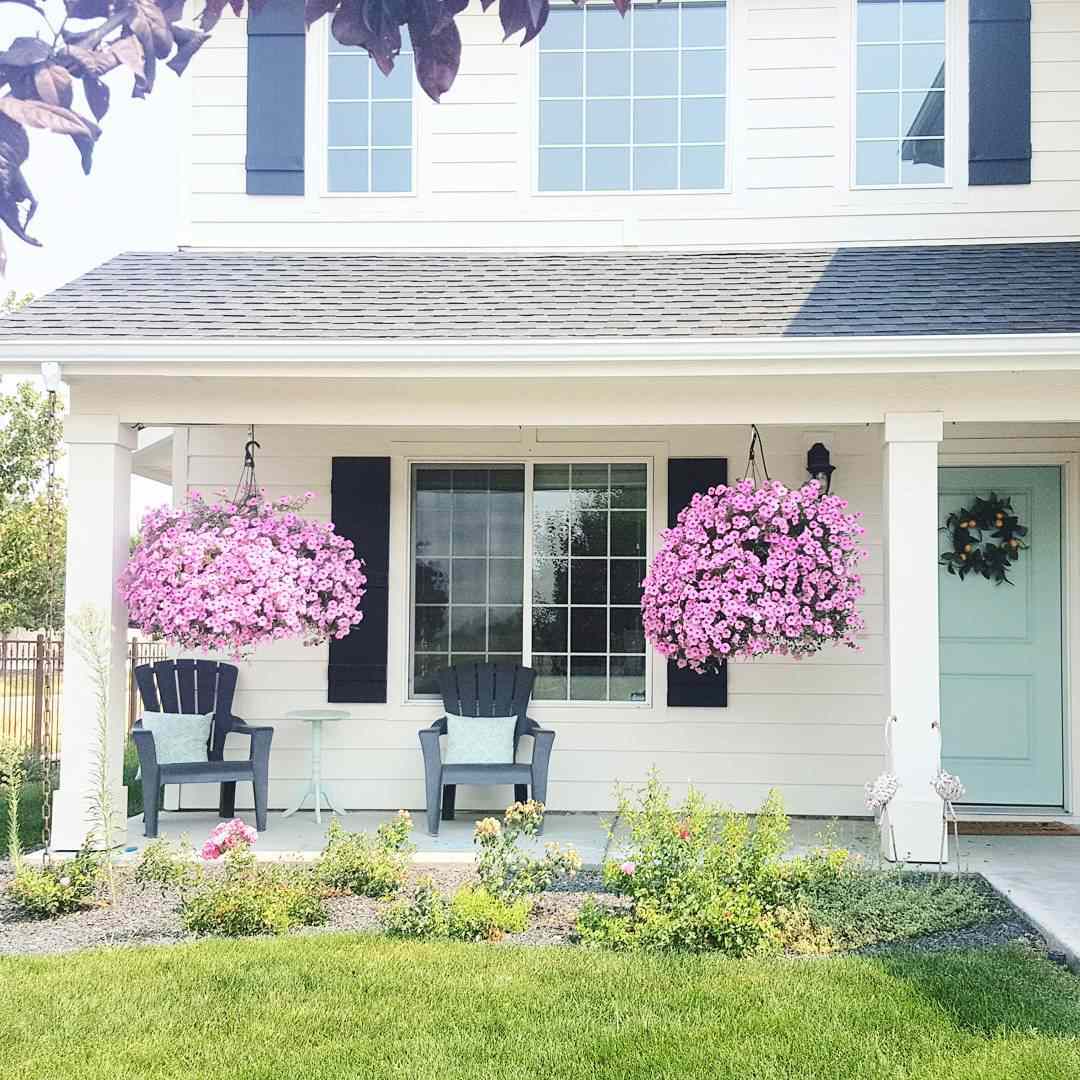 Die Veranda eines Hauses mit einer hellblauen Tür und rosa Blumen.